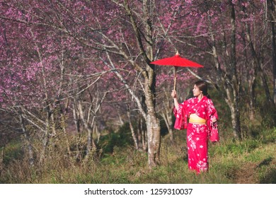 桜の花を背景に着物と赤い和傘を着けたアジアの女性