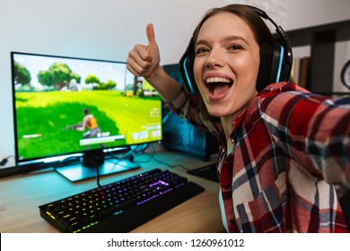 Opgewonden meisjesgamer die aan tafel zit, online games speelt op een computer binnenshuis, een selfie maakt