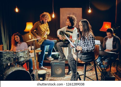 自宅スタジオでのバンド練習。バンドの他のメンバーが楽器を演奏しながら歌っている女性。