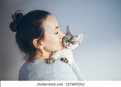 かわいいデボンレックスの猫を抱きしめ、かわいがり、キスをしているカジュアルな服装の女性のライフスタイル写真。子猫は女の子の腕の中にいることを楽しんでいます。セレクティブ フォーカス。
