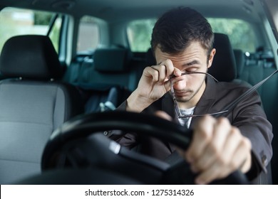 Un joven somnoliento se frota los ojos con la mano derecha. Su mano izquierda está en el volante. Él está sentado en su coche. Concepto de seguridad vial.