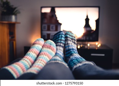 Couple with socks and woolen stockings watching movies or series on tv in winter. Woman and man sitting or lying together on sofa couch in home living room using online streaming service in television