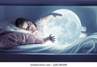 Little girl holding the moon, while lying in bed