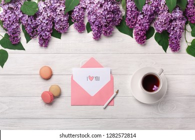 Sejambak bunga ungu, secawan teh, nota cinta dan makaroni di atas meja kayu putih. Pandangan atas dengan tempat untuk tahniah anda.