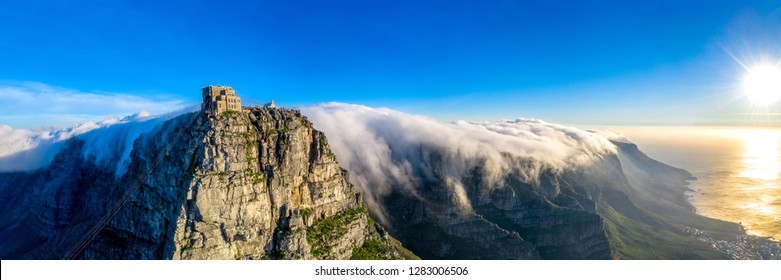 Tafelberg-kabelbaan bedek met wolke wat oor die twaalf apostels vee tydens sonsondergang in Kaapstad