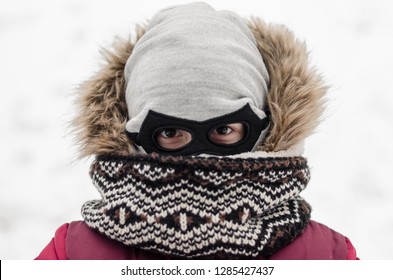 Little boy face covered with a hat as a batman mask. Winter season and snowing weather. Dark eyes of a little kid.