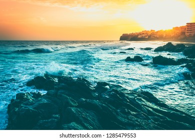 グラン カナリア島のプラヤ デル アギラの海沿いのアパートの丘の背後にある素晴らしい夕暮れ。カナリア諸島、スペインの岩に波がしぶきを上げた幻想的な夕日