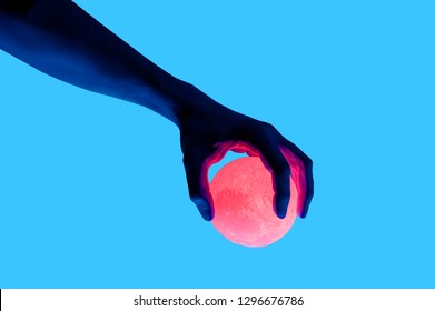 Foto terisolasi pada latar belakang biru seorang pria memegang bola bercahaya berbentuk bulan. Gaya kolase surealis, elemen seni kontemporer untuk desain, poster, dan spanduk. Cahaya ungu neon. Inspirasi pop