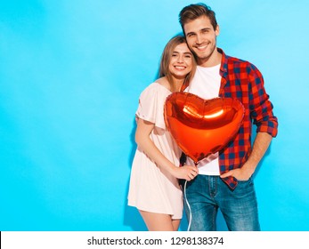 Portrait d'une belle fille souriante et de son beau petit ami tenant des ballons à air en forme de cœur et riant. Famille heureuse. Amour. Joyeuse Saint-Valentin. Isolé sur un mur bleu
