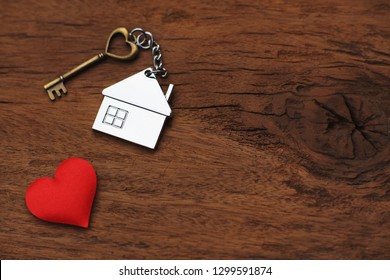 Chave da casa com chaveiro de casa decorado com mini coração vermelho em fundo de textura de madeira, conceito de casa doce, espaço de cópia