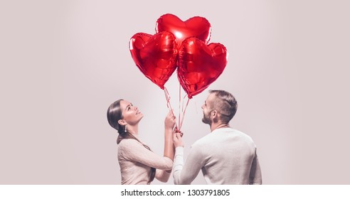 Pareja de San Valentín. Retrato de la chica de belleza sonriente y su novio guapo sosteniendo un montón de globos de aire en forma de corazón y riendo. Familia alegre feliz. Amor. Feliz día de San Valentín