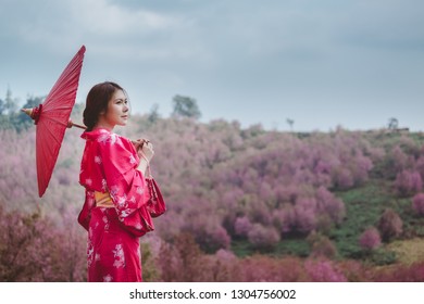 桜の花を背景に着物と赤い和傘を着けたアジアの女性
