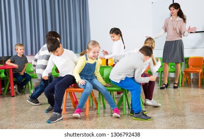 Happy laughing pupils of primary school having fun during break with their teacher, playing musical chairs