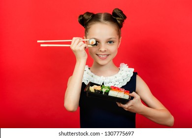 Cute smiling little girl with with sushi on red background. Student child girl eating sushi and rolls - commercial concept.