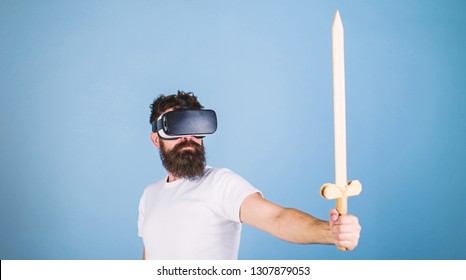 Gamer-concept. Man met op het hoofd gemonteerd display houdt zwaard vast, speel vechtspel in VR. Hipster op serieus gezicht geniet van het spelen van games in virtual reality. Man met baard in Vr-bril, lichtblauwe achtergrond.