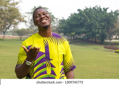 Een afrikaanse man in een open veld van groen gras en heldere luchten opent de hand naar de hemel in blije opluchting en glimlacht.