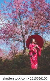 桜の花を背景に着物と赤い和傘を着けたアジアの女性