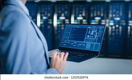サーバー ラックの横にあるデータ センターでラップトップに取り組んでいる IT スペシャリストの背面ビューのクローズ アップ ショット。コンピュータは診断を実行しているか、メンテナンス作業を行っています。