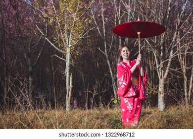 桜の花を背景に着物と赤い和傘を着けたアジアの女性