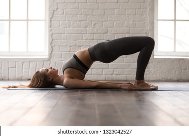 Junge sportliche Frau in grauer Sportbekleidung, Leggings und BH, die Yoga praktizieren, schönes Mädchen, das Glute-Bridge-Übung macht, dvi pada pithasana Pose, zu Hause oder im Yoga-Studio trainierend