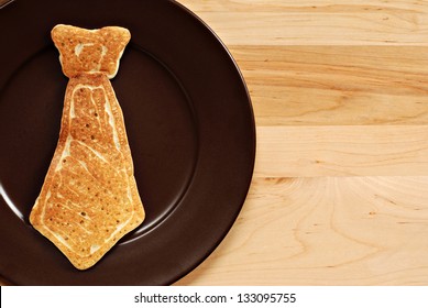 Vatertags-Hintergrundbild mit echtem Pfannkuchen in Form einer Krawatte auf Teller. Nahaufnahme mit hölzernem Hintergrund und Kopienraum.