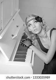 Joven actriz con ojos azules mirando hacia arriba mientras está acostada sobre un teclado abierto de piano blanco.