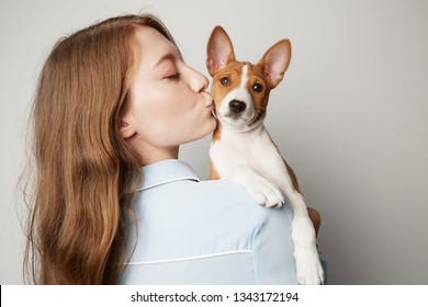 Knappe roodharige jonge vrouw knuffelen en kussen van haar puppy basenji hond. Liefde tussen hond en baasje. Geïsoleerd op een witte achtergrond.