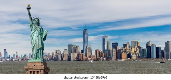 Pemandangan panorama Patung Liberty dengan One World Trade Center dan pencakar langit pusat kota Manhattan dengan latar langit biru awan, distrik Keuangan Manhattan bawah, Kota New York, AS.
