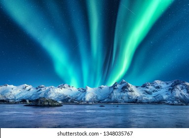 Aurora borealis di atas pegunungan yang tertutup salju di pulau Lofoten, Norwegia. Cahaya utara di musim dingin. Pemandangan malam dengan lampu kutub, batu bersalju, refleksi di laut. Langit berbintang dengan aurora