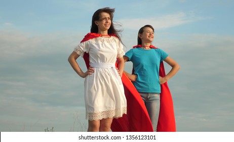 Mom and daughter play superheroes. two girls in red cloaks of superheroes stand against blue sky, the wind inflates a cloak. happy family concept