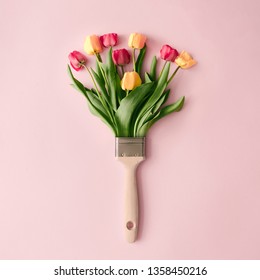 Kreatives Frühlingskonzept mit Pinsel und bunten Tulpenblumen auf pastellrosa Hintergrund. Minimale Naturflachlage.