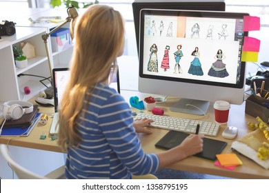 Mặt sau của nữ nhà thiết kế thời trang tóc vàng trẻ tuổi người da trắng sử dụng máy tính bảng đồ họa khi làm việc tại bàn làm việc trong một văn phòng hiện đại