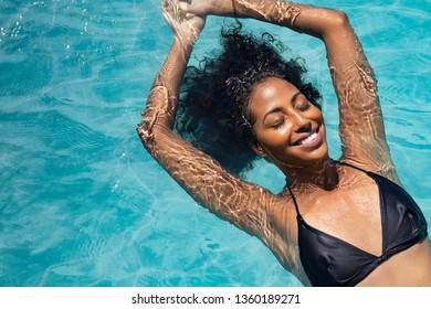 Blick aus der Vogelperspektive auf eine schwarze Frau, die sich mit geschlossenen Augen im Wasser entspannt. Porträt einer glücklichen Frau im Bikini, der in einem Wasser schwimmt. Draufsicht auf entspanntes afrikanisches Mädchen im Schwimmbad mit Kopierraum.
