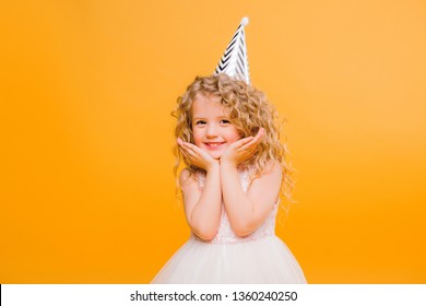 Young blond girl in birthday party princess hat hands spread up screaming isolated on a yellow background,Young beautiful girl wearing birthday cap over isolated background smiling with happy face