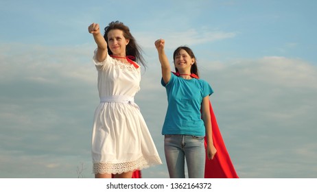 teamwork superheroes. two girls in red cloaks of superheroes stand against a blue sky, the wind inflates cloak. Mom and daughter play superheroes. happy family concept.