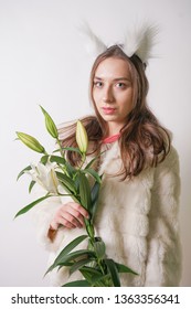 cute young teen girl standing in a winter warm fur coat and cat furry ears on her head, she holds a branch of fresh lilies. woman in winter clothes with a flower on a white background in the Studio.