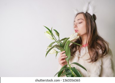 cute young teen girl standing in a winter warm fur coat and cat furry ears on her head, she holds a branch of fresh lilies. woman in winter clothes with a flower on a white background in the Studio.