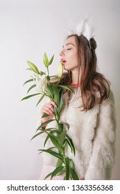 cute young teen girl standing in a winter warm fur coat and cat furry ears on her head, she holds a branch of fresh lilies. woman in winter clothes with a flower on a white background in the Studio.