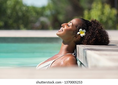 Young black woman relaxing at spa pool. Beautiful woman relaxing in outdoor spa swimming pool with head leaning at poolside. Closeup face of attractive girl with closed eyes enjoy vacation at resort.