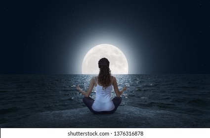 Mujer joven meditando en pose de loto en la playa del mar en la noche de luna llena