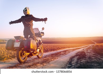 Motorbiker travelling, autumn day, motorcycle off road, the driver stands with open arms to the side, to meet a new day, adventurer, extreme tourism, cold weather clothes, light tinting
