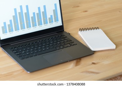 ノートブックのモックアップと、ノートブック、スマートフォン、メモ帳、サボテンの植物を備えたオフィスの木製テーブル。デスクトップのモックアップとビジネス デスクトップ シーン。画面に販売グラフィックが表示された暗いノート。