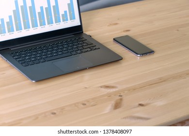 Maqueta de portátil y mesa de madera de oficina con portátil, smartphone, bloc de notas y planta de cactus. Maqueta de escritorio y escena de escritorio empresarial. Cuaderno oscuro con gráfico de ventas en pantalla.