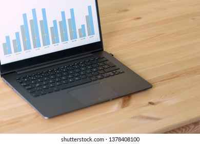 ノートブックのモックアップと、ノートブック、スマートフォン、メモ帳、サボテンの植物を備えたオフィスの木製テーブル。デスクトップのモックアップとビジネス デスクトップ シーン。画面に販売グラフィックが表示された暗いノート。