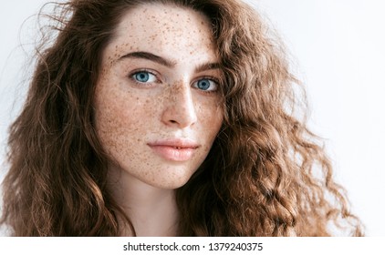 Beautiful Freckles young woman close up portrait. Attractive model with beautiful blue eyes and ginger curly hair 