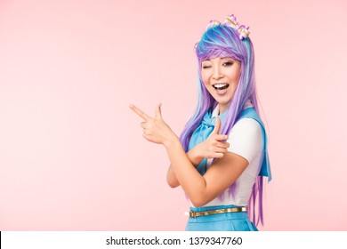 Vajzë e gëzueshme anime me paruke ngjyrë vjollce që tregon me gishta dhe bën syrin e izoluar në rozë