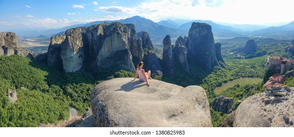 DRONE: Mujer joven sentada en un acantilado y observa el antiguo monasterio griego. Chica intrépida e irreconocible de vacaciones de verano en Grecia sentada en un acantilado y observando las formaciones rocosas de Meteora.
