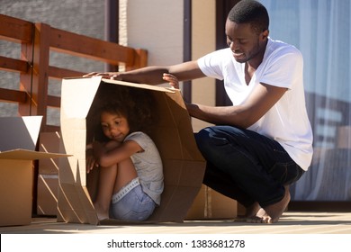 Jonge Afro-Amerikaanse vader speelt met kleine dochter buiten het nieuwe huis op verhuisdag, zwarte duizendjarige vader heeft plezier met klein kind, verstopt zich in kartonnen doos en verhuist graag naar zijn eigen huis