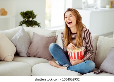 صورة مقربة جميلة لها نموذج سيدة يداها حاوية كبيرة ذرة أذرع تضحك بصوت عالٍ كوميدي مسلسل وجبات سريعة ترتدي جينز جينز مخطط سترة ملابس تجلس مريحة أريكة منزل غرفة المعيشة في الداخل