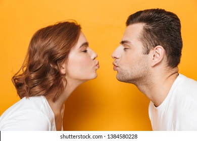 Cerca de una hermosa pareja con camisetas blancas que se encuentran aisladas sobre un fondo amarillo, besándose